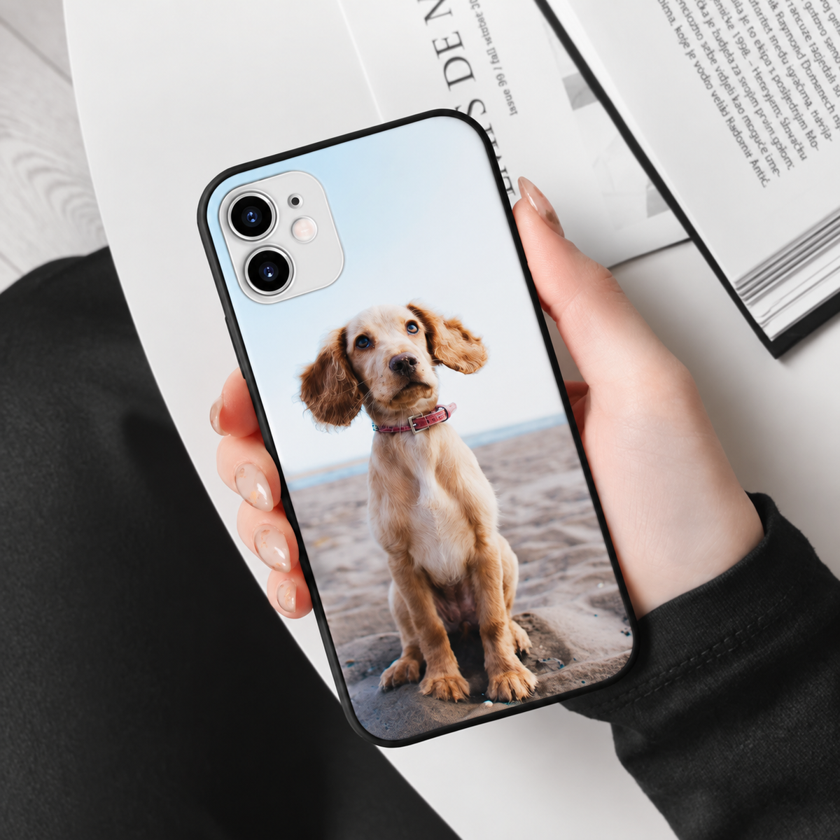 Coque de téléphone noire personnalisée avec photo d'un chien, tenue par une personne.