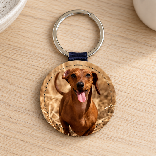 Ronde sleutelhanger met foto van een lachende hond op een houten tafel.