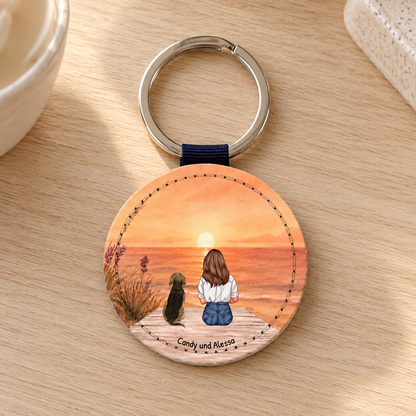Gepersonaliseerde ronde sleutelhanger met illustratie van een vrouw en een hond bij zonsondergang.