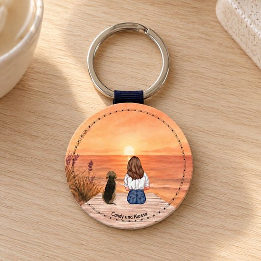Gepersonaliseerde ronde sleutelhanger met illustratie van een vrouw en een hond bij zonsondergang.