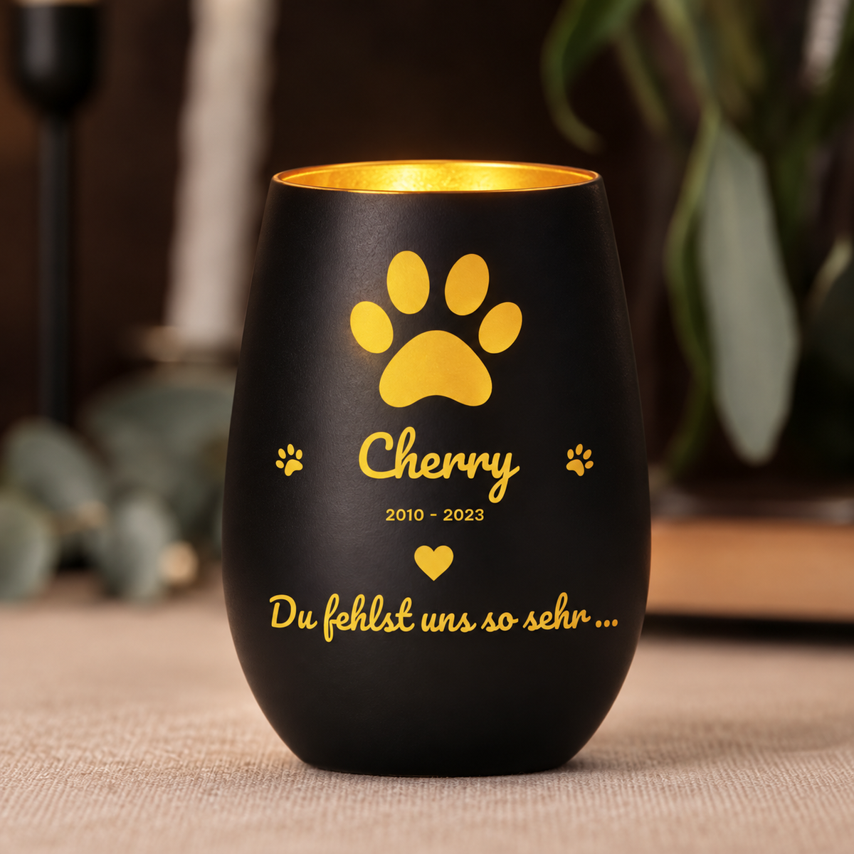Zwart herdenkingslicht met gouden tekst en pootafdrukken, gepersonaliseerd met naam en jaar.