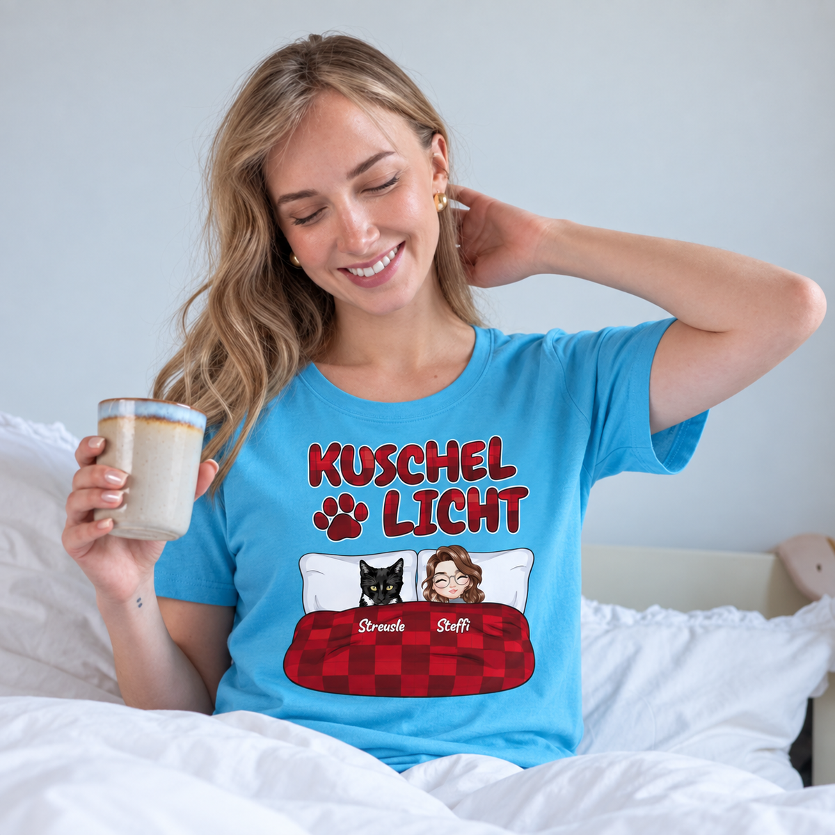T-shirt turquoise avec l'inscription "Kuschel Licht", porté par une femme souriante au lit.