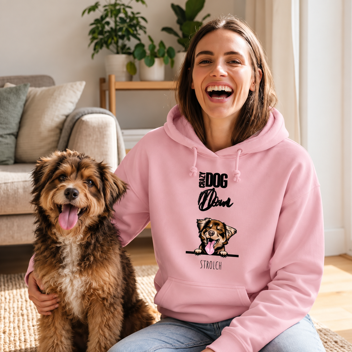 Lachende vrouw in roze hoodie met hondenmotief, zit naast een hond op een vloerkleed.