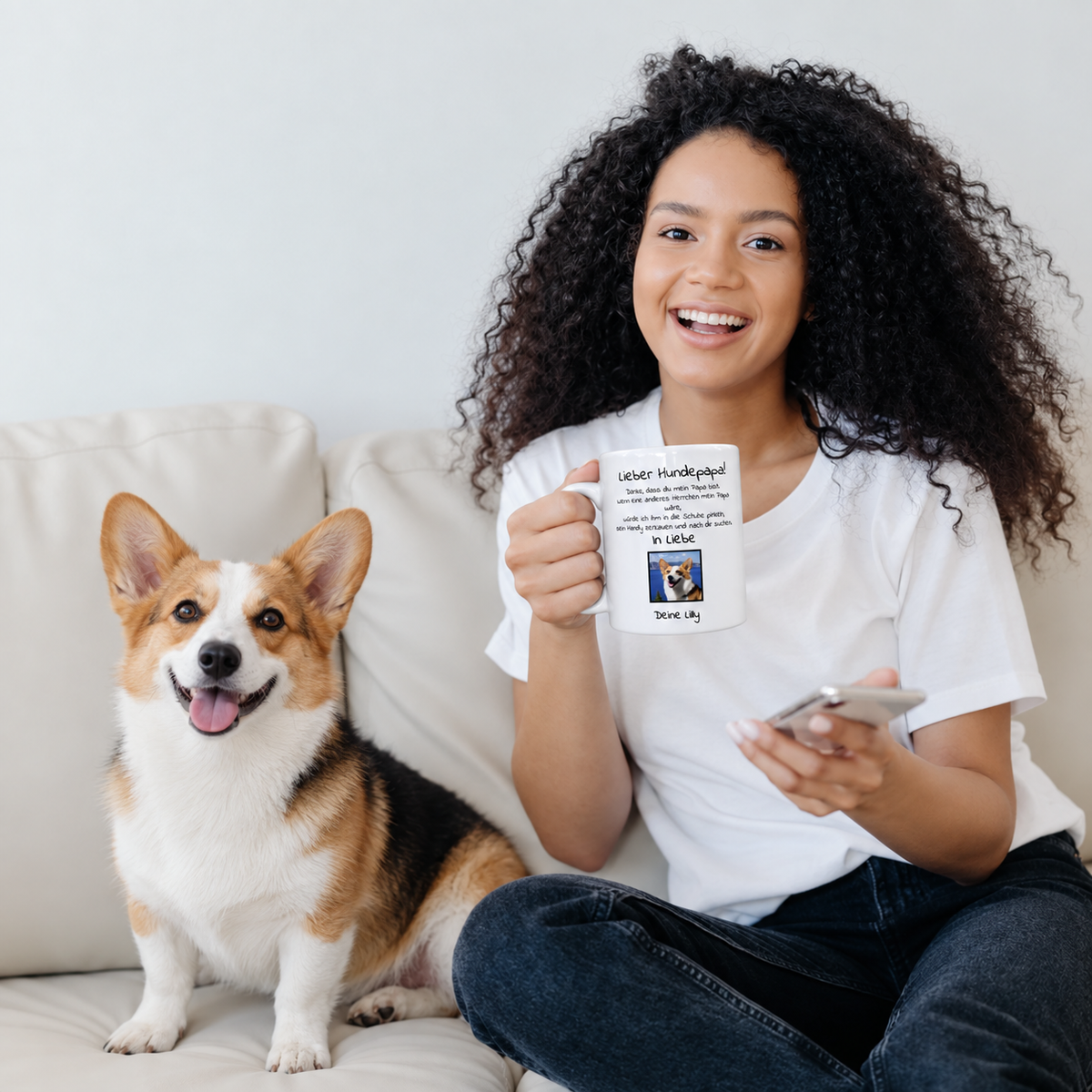 Personne tenant un mug personnalisé avec l'inscription "Lieber Hundepapa" et photo, assise sur un canapé à côté d'un chien.