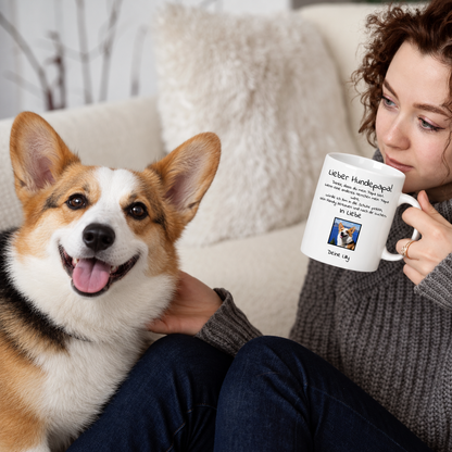 Personne buvant dans un mug blanc avec l'inscription "Lieber Hundepapa", un chien assis à côté.