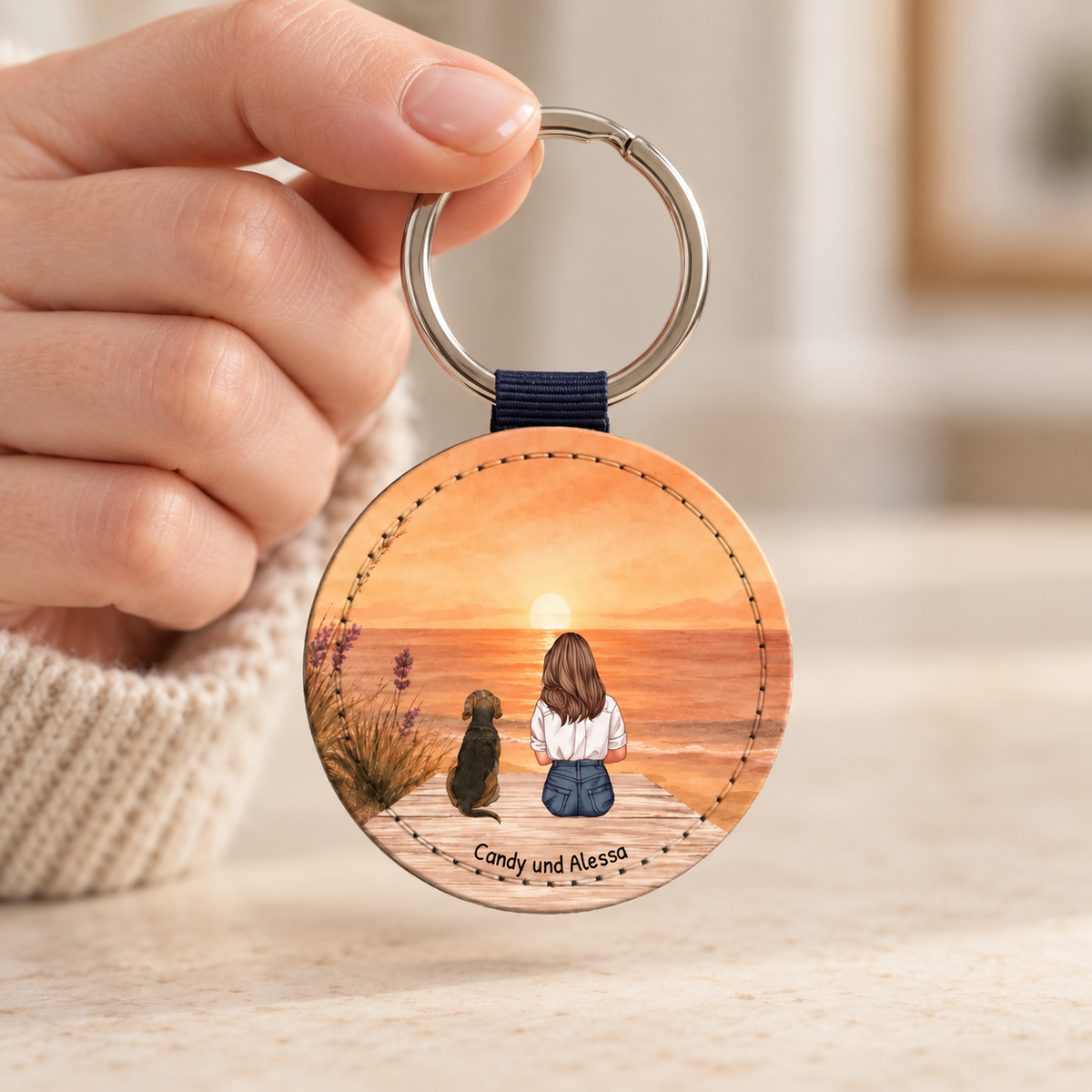 Gepersonaliseerde ronde sleutelhanger met illustratie van een persoon en hond aan zee bij zonsondergang.