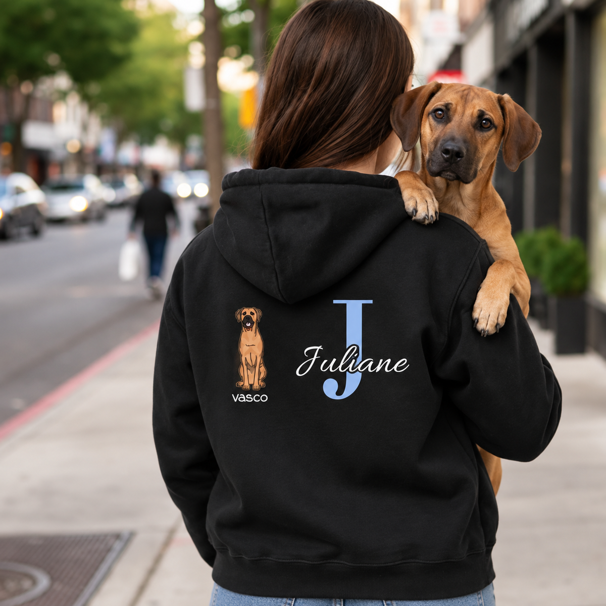 Zwarte hoodie met gepersonaliseerde initiaal "J" en hondenmotief op de rug. Gedragen door iemand met een hond.