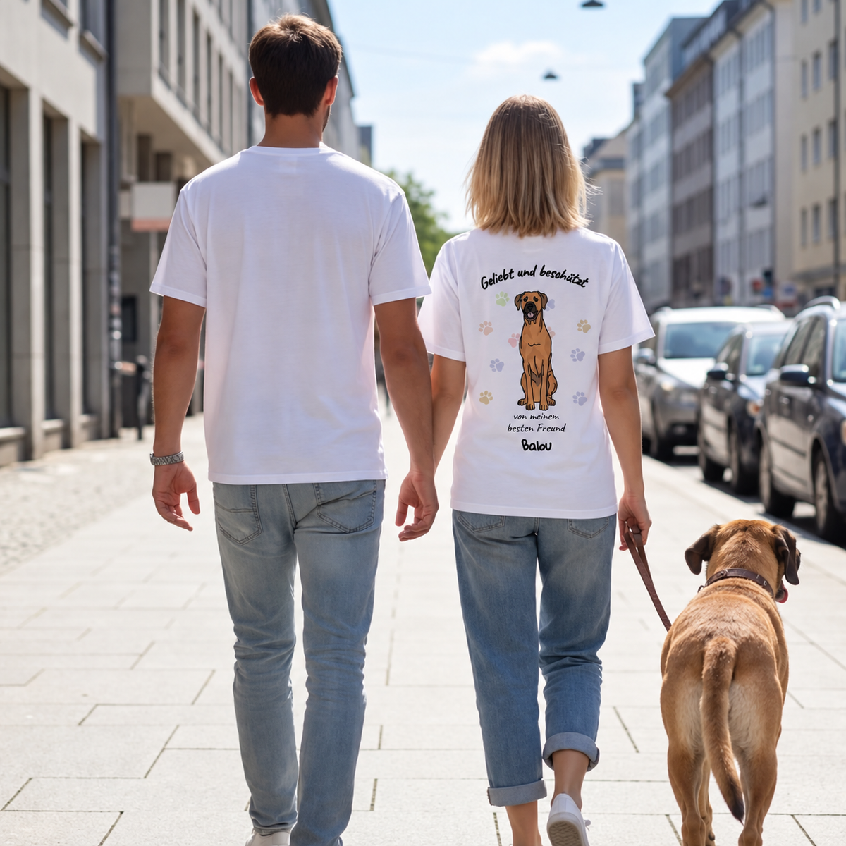 Deux personnes en T-shirts blancs avec motif de chien au dos, promenant un chien.
