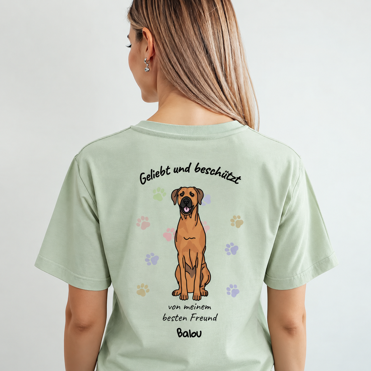 T-shirt vert clair avec imprimé chien et le texte "Geliebt und beschützt" au dos.