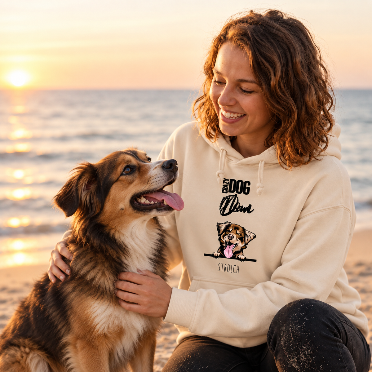 Beige hoodie met hondenmotief, gedragen door iemand op het strand bij zonsondergang.