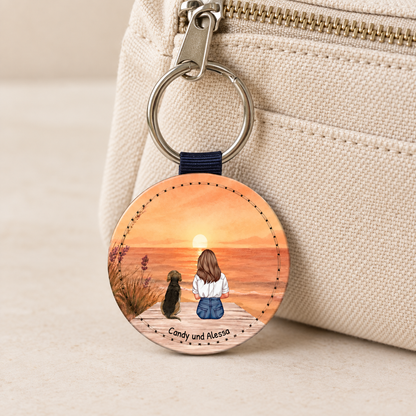Gepersonaliseerde sleutelhanger met illustratie van een vrouw en een hond voor een zonsondergang.