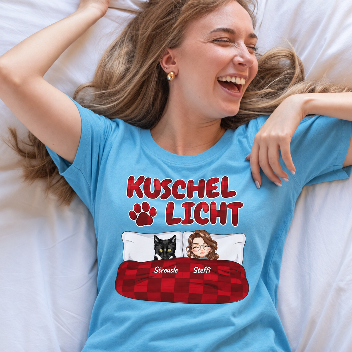 T-shirt bleu avec l'inscription "Kuschel Licht" et éléments graphiques de deux personnes et d'un animal noir.