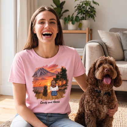 Roze T-shirt met gepersonaliseerde print van een vrouw en twee honden voor een landschap bij zonsondergang.
