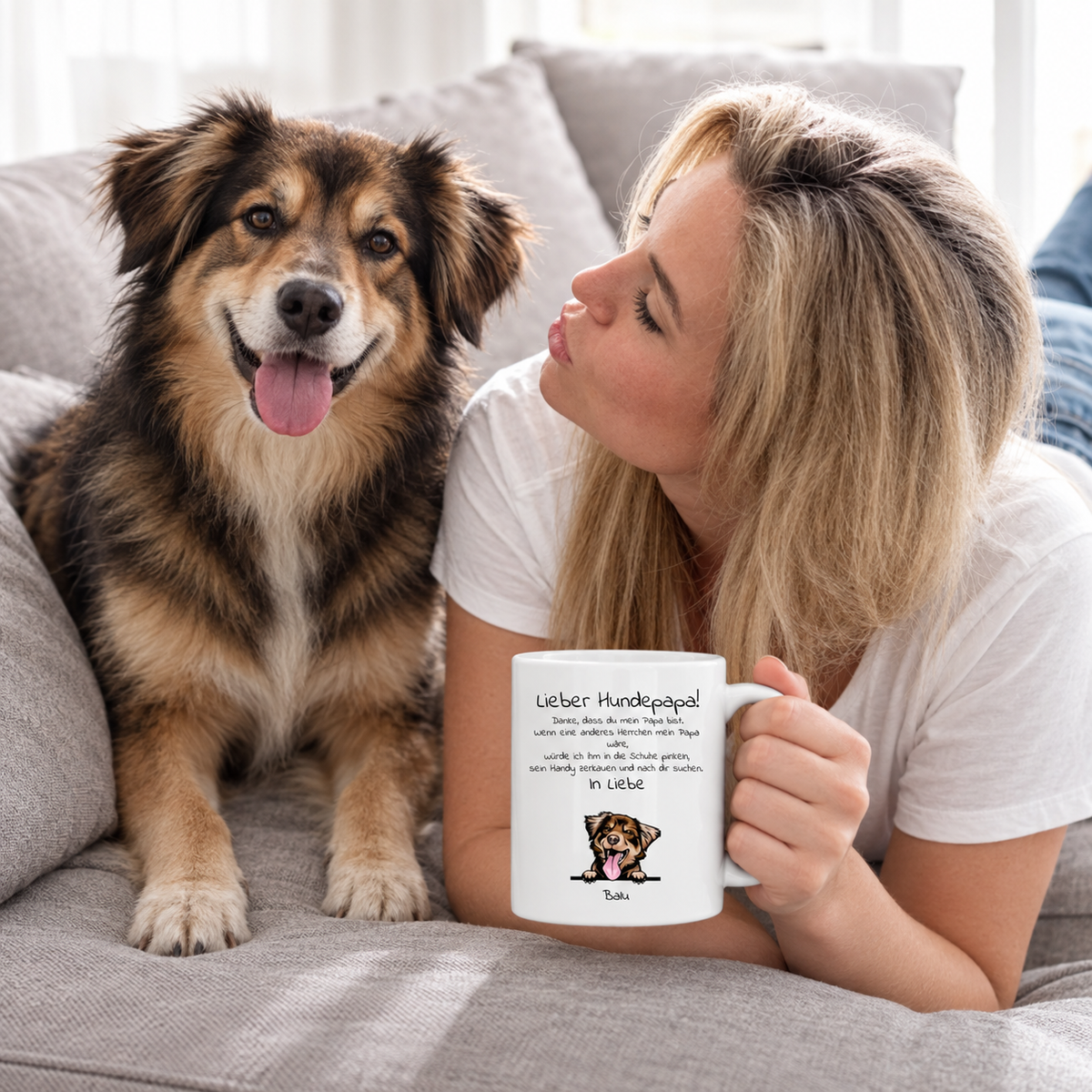 Vrouw met gepersonaliseerde mok "Lieber Hundepapa" en hond op een grijze bank. Witte mok met tekst en illustratie.