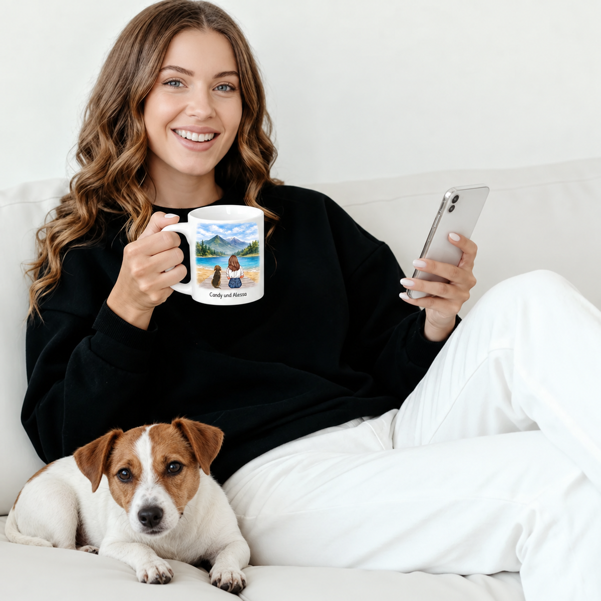 Persoon houdt een gepersonaliseerde mok met landschapsmotief vast, naast haar ligt een hond op de bank.