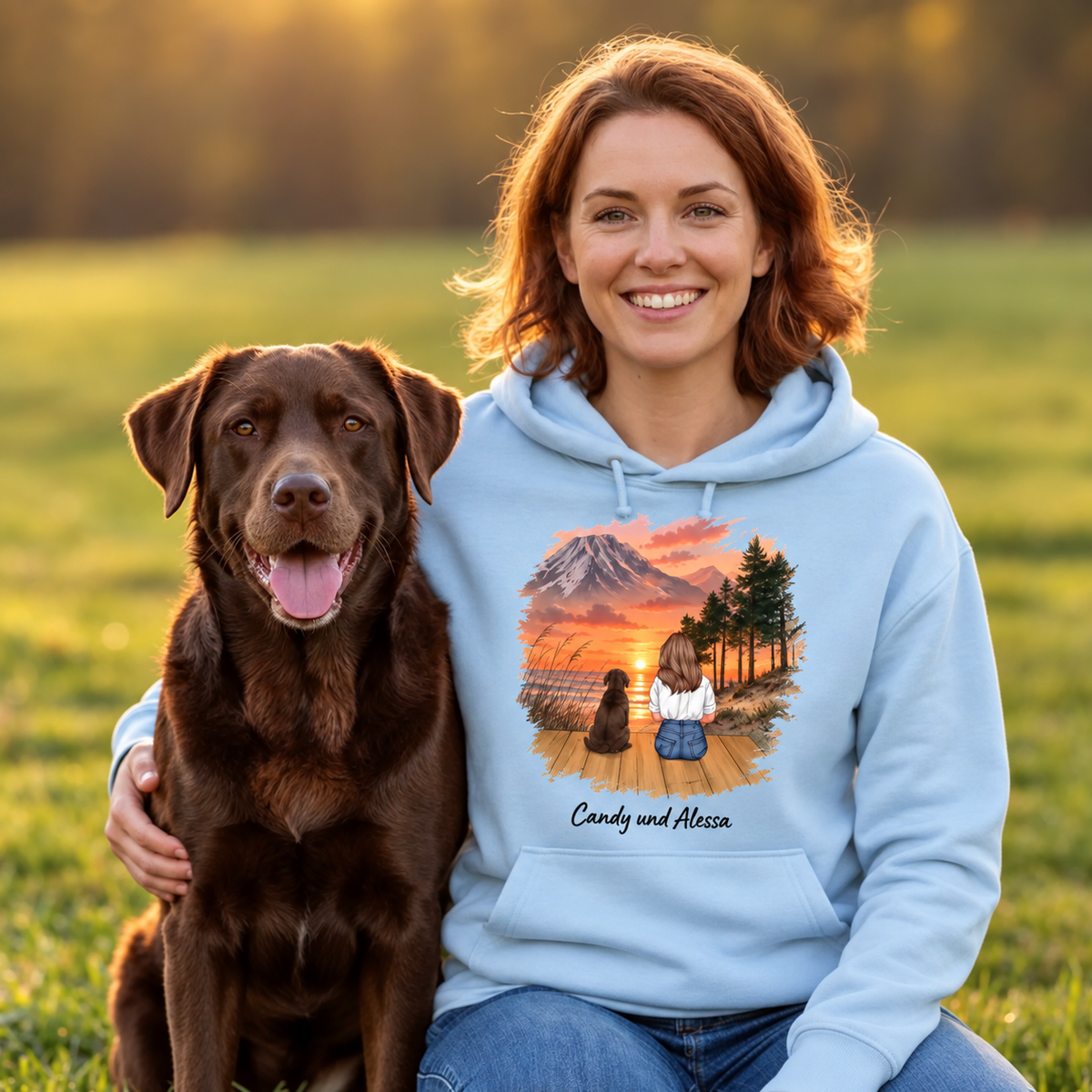 Veste à capuche bleu clair avec illustration d'une personne et d'un chien devant un paysage au coucher du soleil.