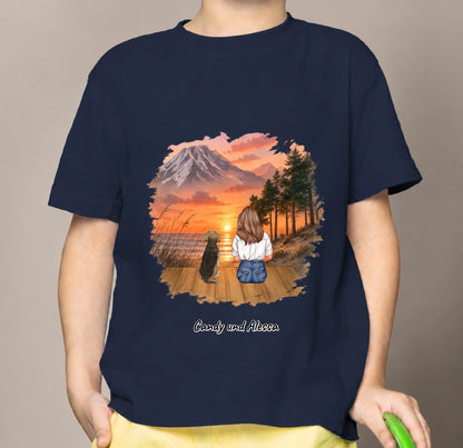 Blauw kindershirt met afbeelding van een zittende persoon en hond in een zonsonderganglandschap.