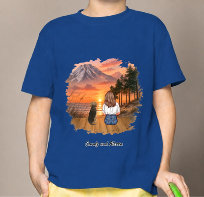 Blauw kindershirt met illustratie van een meisje en hond die naar een zonsondergang kijken.