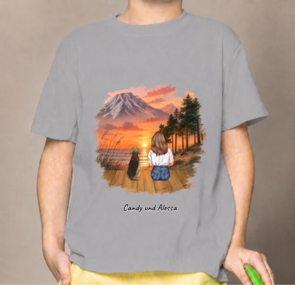 Grijs kindershirt met afbeelding van een zittende persoon en een hond bij zonsondergang.