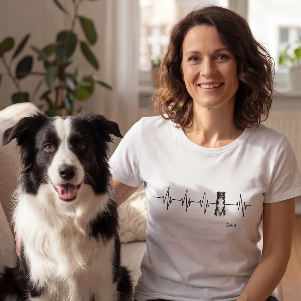 Wit T-shirt met hartslagontwerp en hondenmotief, personalisatie mogelijk. Vrouw zit met hond op een bank.