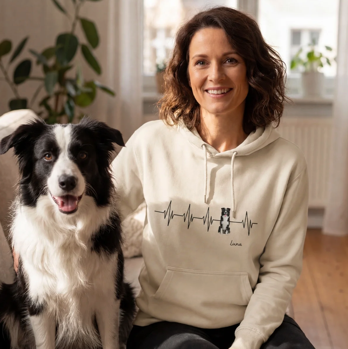 Sweat à capuche beige avec motif battement de cœur et inscription personnalisée, porté par une femme à côté d'un chien.