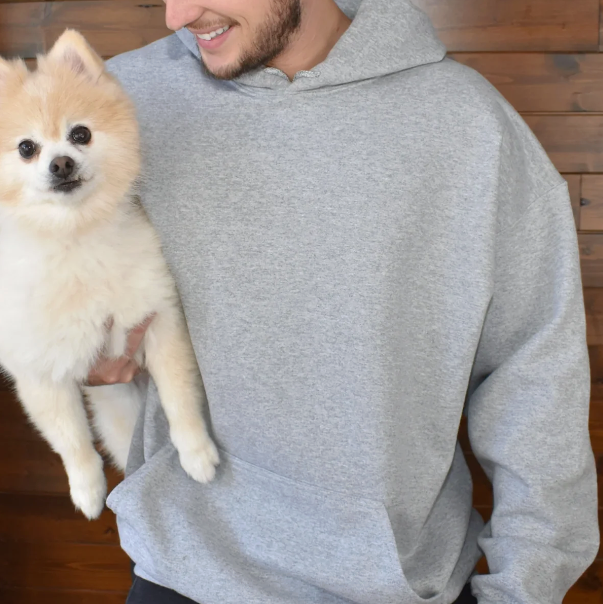 Grijze hoodie met grote capuchon, gedragen door iemand die een dwergkeeshond draagt.