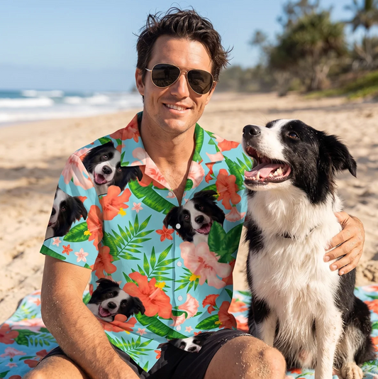 Man met zonnebril in een gepersonaliseerd Hawaï-overhemd met hondenmotieven, zit op het strand naast een hond.