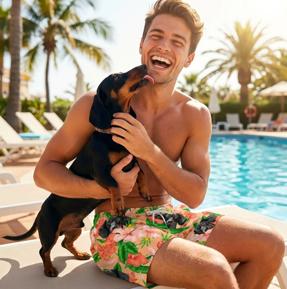 Man met zwarte hond zit bij het zwembad, in een kleurrijke zwembroek met bloemen- en hondenpatroon.
