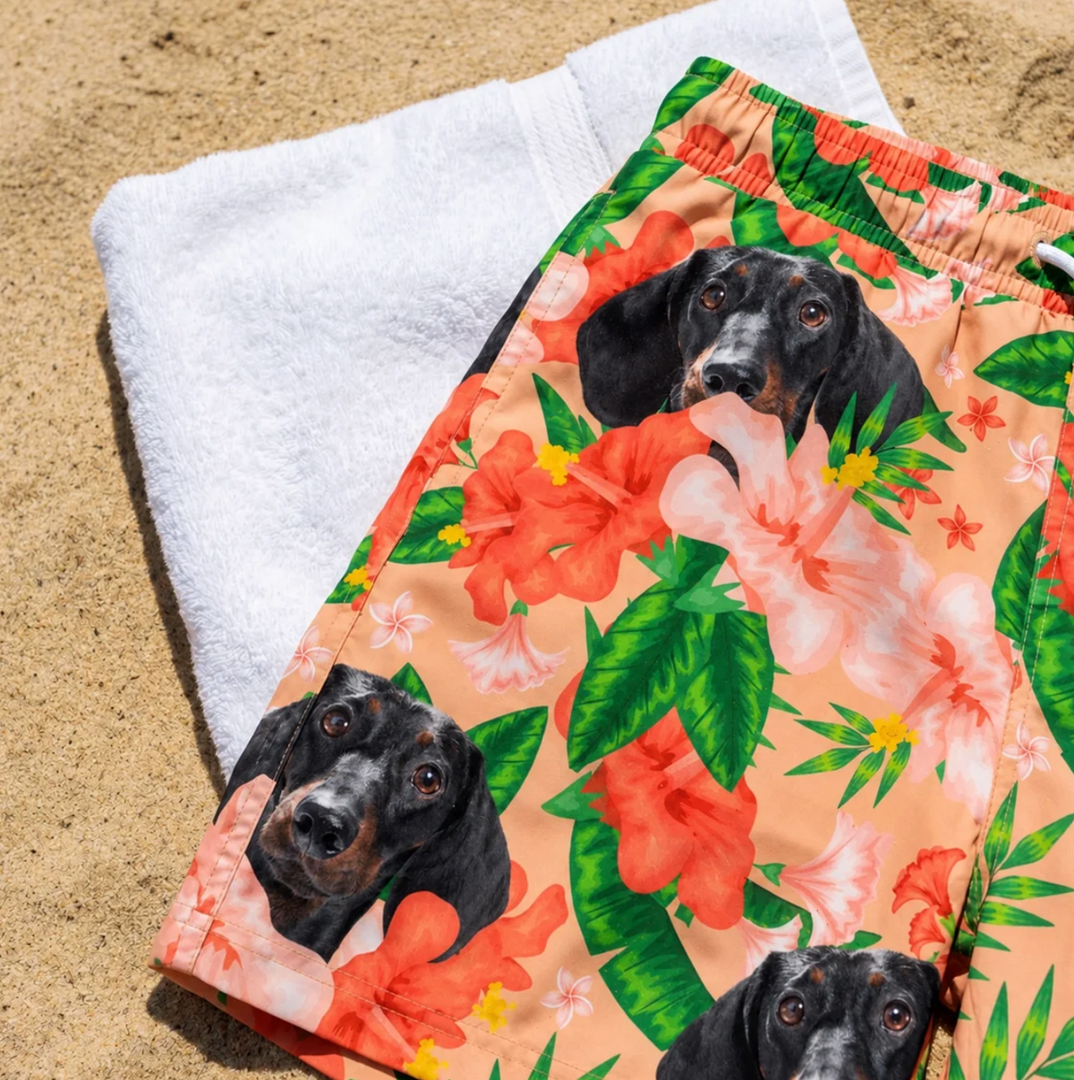 Gepersonaliseerde zwembroek met bloemenmotieven en hondenprint, liggend op een zandstrand.