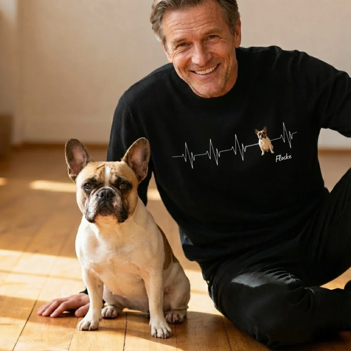 Gepersonaliseerde zwarte sweater met hartslagmotief en hondenfoto. Een man zit naast een hond.