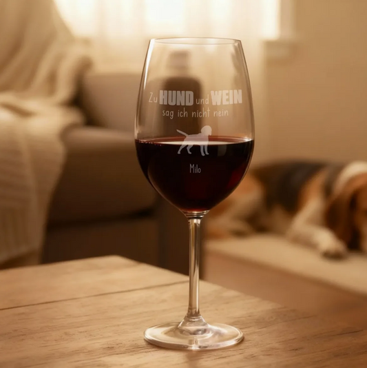 Gepersonaliseerd gegraveerd wijnglas gevuld met rode wijn, met hondenmotief en naam, op een houten tafel.