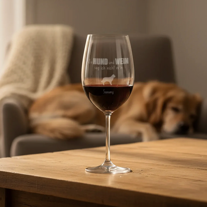 Verre à vin gravé personnalisé rempli de vin rouge, au premier plan sur une table en bois. Chien en arrière-plan.