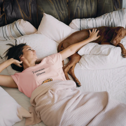 Vrouw in roze T-shirt ligt op bed naast een hond, omringd door kussens en een deken.