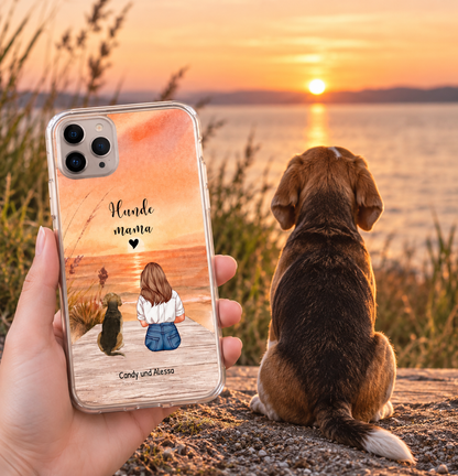 Transparant telefoonhoesje met kunstmotief van een persoon en hond op het strand bij zonsondergang.