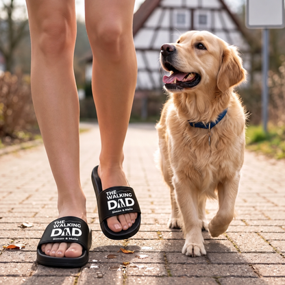 Zwarte badslippers met opdruk "THE WALKING DAD", gedragen tijdens een wandeling met een golden retriever.
