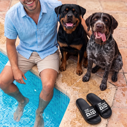 Gepersonaliseerde zwarte badslippers met opdruk "THE WALKING DAD", naast een man en twee honden bij het zwembad.
